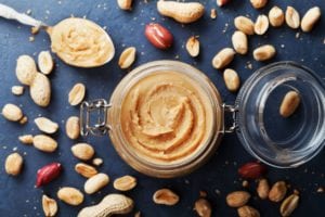 A jar of peanut butter surrounded by peanuts.